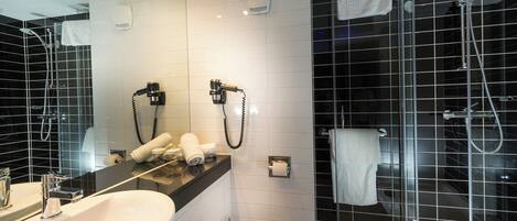 Un baño moderno con un espejo grande, un lavamanos blanco, un inodoro y una zona de ducha con mampara de vidrio.