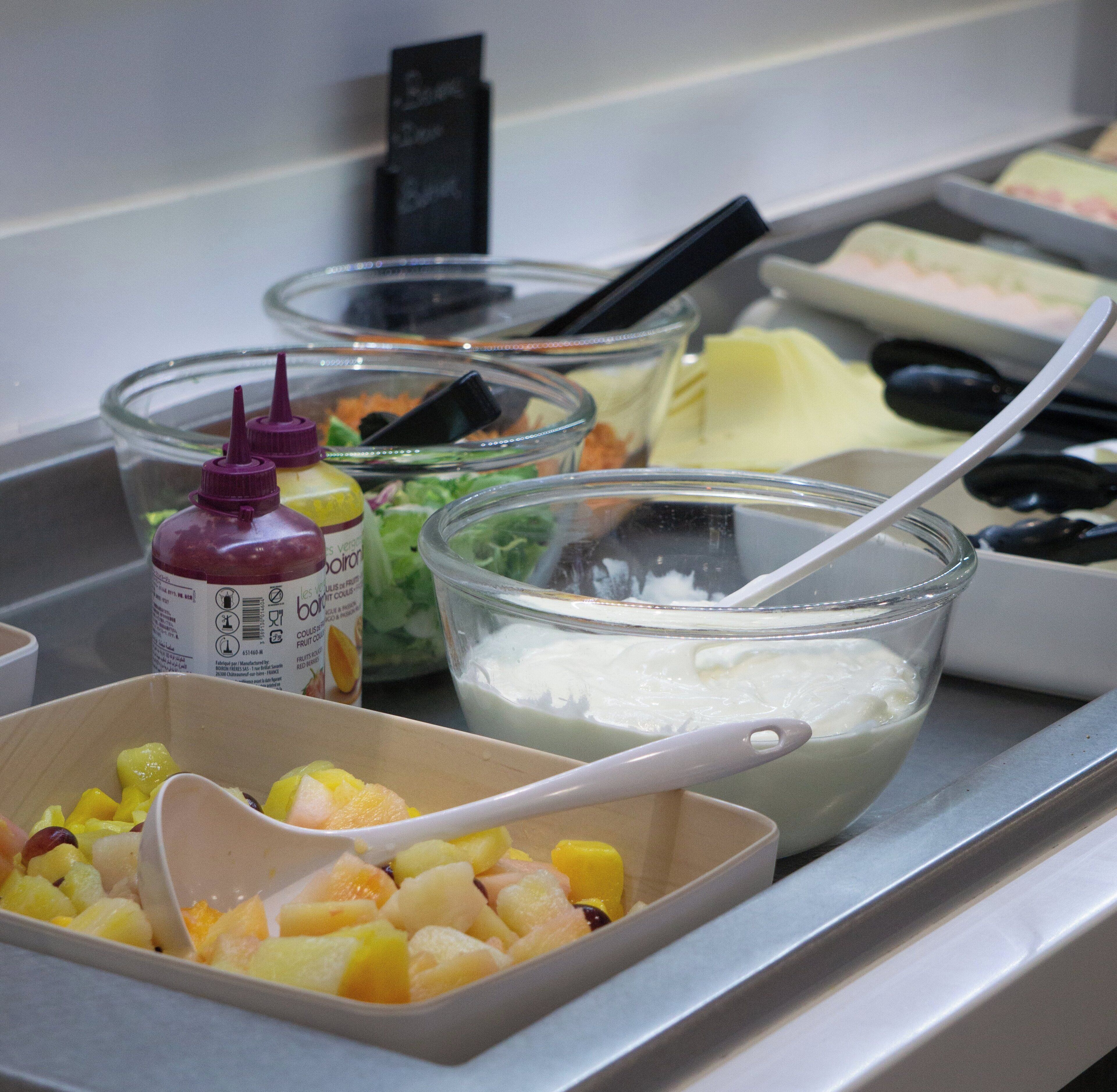 A buffet with various food items including fruits, a bowl of yogurt, and condiments.