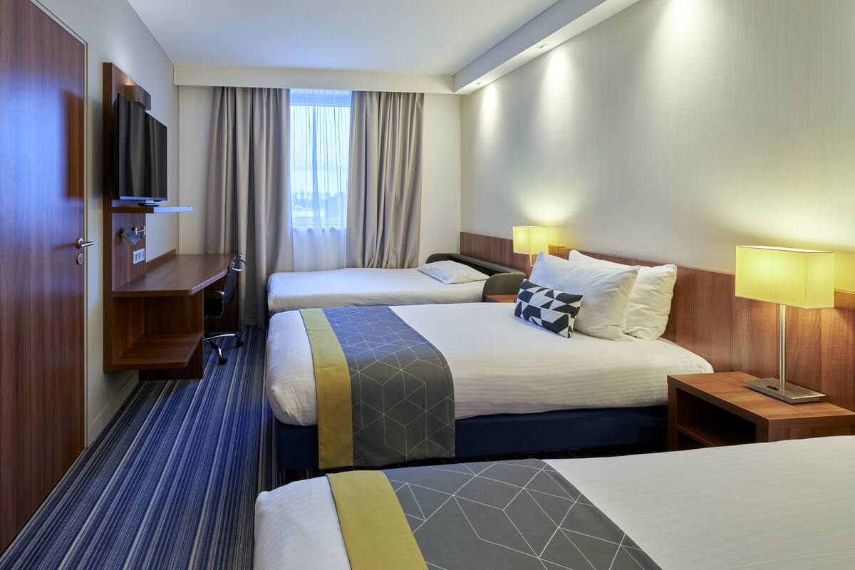 A hotel room with two beds, a TV, a desk, and a window with curtains.