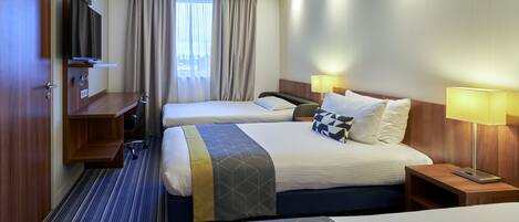 Habitación de hotel con dos camas, televisión, escritorio y ventana con cortinas.