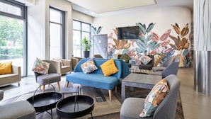 A modern living room with a blue sofa, grey armchairs, and a flat-screen TV mounted on the wall. - Holiday Inn Express Strasbourg - Centre by IHG (Strasbourg)