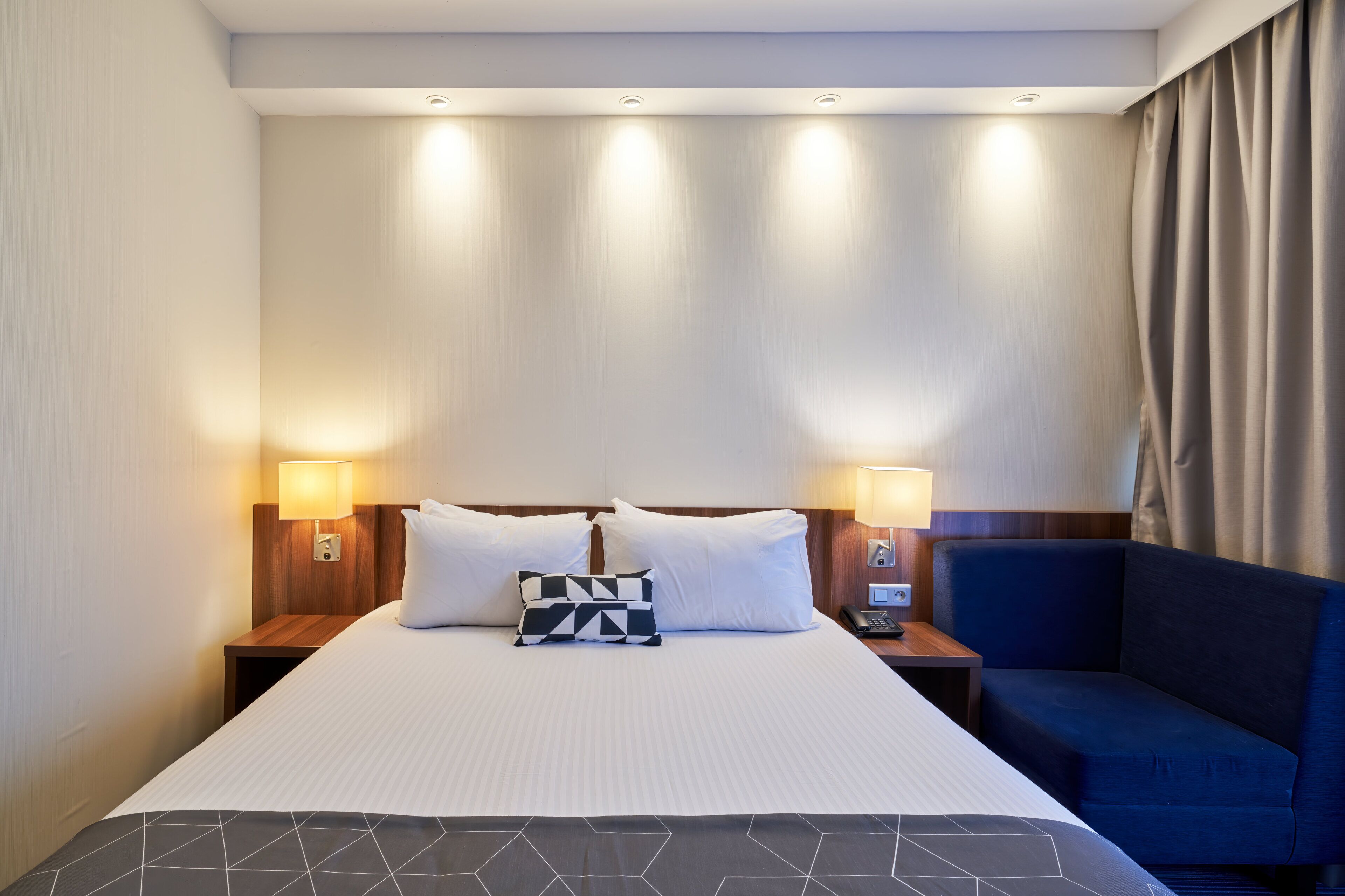 Une chambre d’hôtel avec un grand lit, deux lampes de chevet, un téléphone sur la table de chevet et un fauteuil bleu.