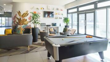 A modern indoor pool area with a pool table, seating, and a TV on the wall.
