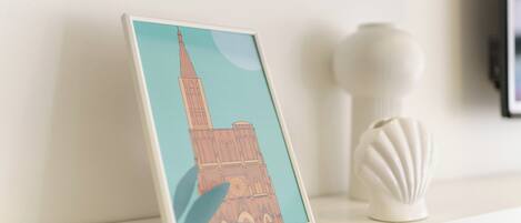 Ein gerahmtes Bild eines Gebäudes mit einem Turm, platziert auf einem Regal neben einer weißen Vase.