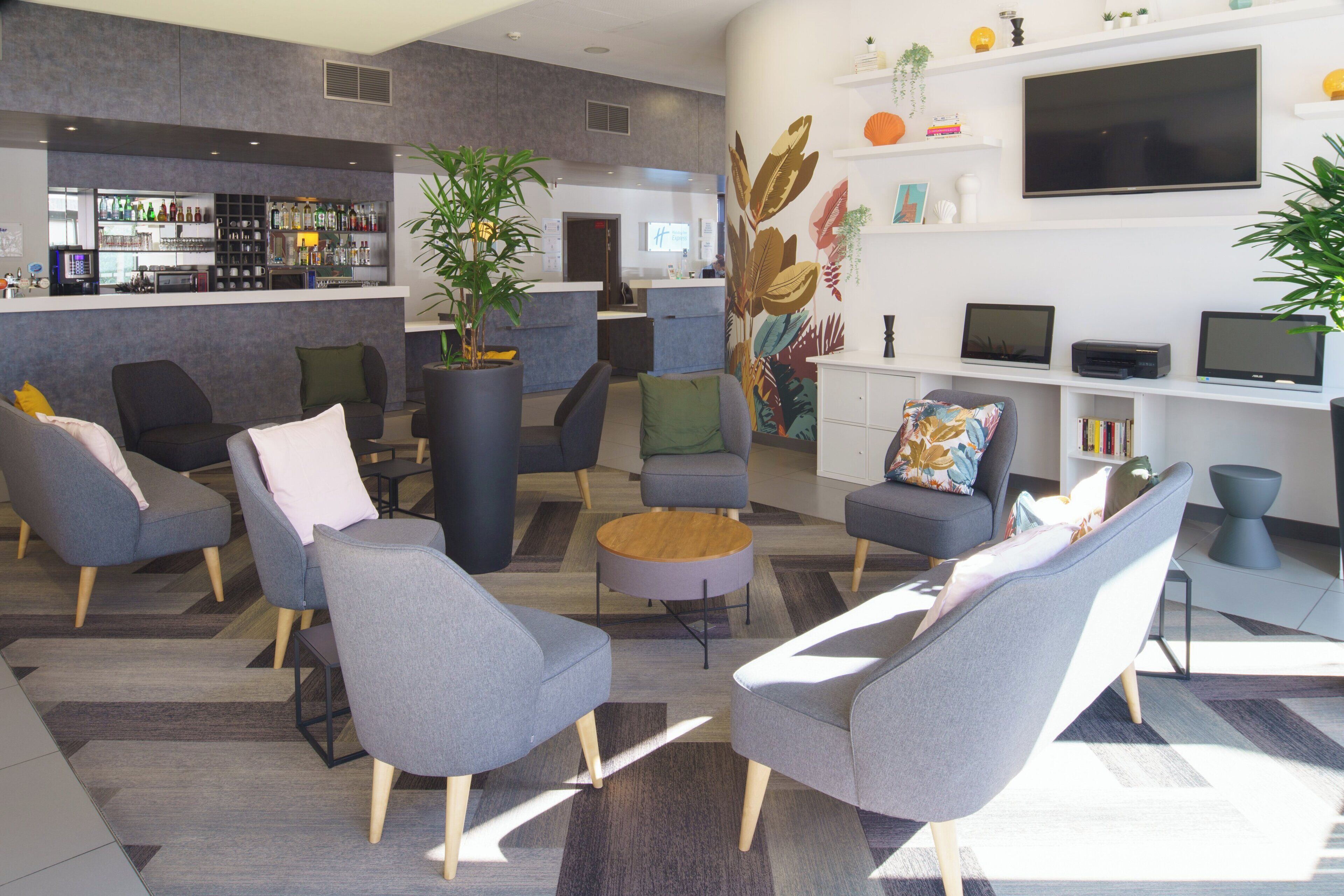 Un espace détente moderne avec des canapés gris, une table basse et un coin bar où sont exposées différentes bouteilles.