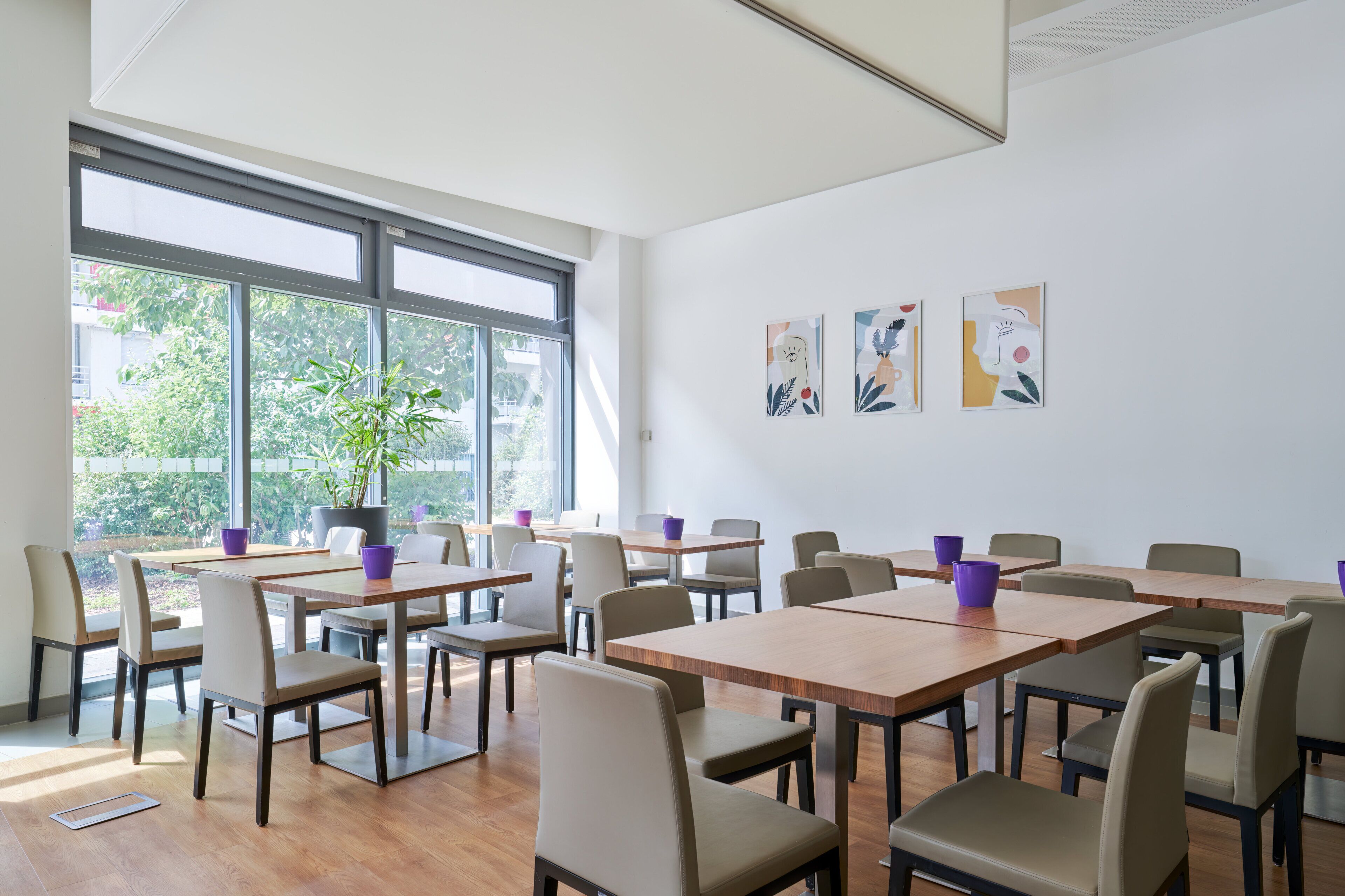 Sala de conferências com várias mesas e cadeiras, grandes janelas com vista para o verde e arte abstrata nas paredes.