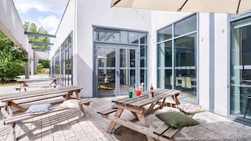 An outdoor patio area with wooden picnic tables, a pergola, and a glass building with sliding doors.