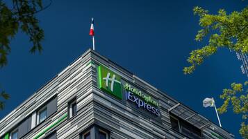 Un edificio moderno con un letrero de Holiday Inn Express, que presenta un asta con una bandera y un cielo azul despejado al fondo.