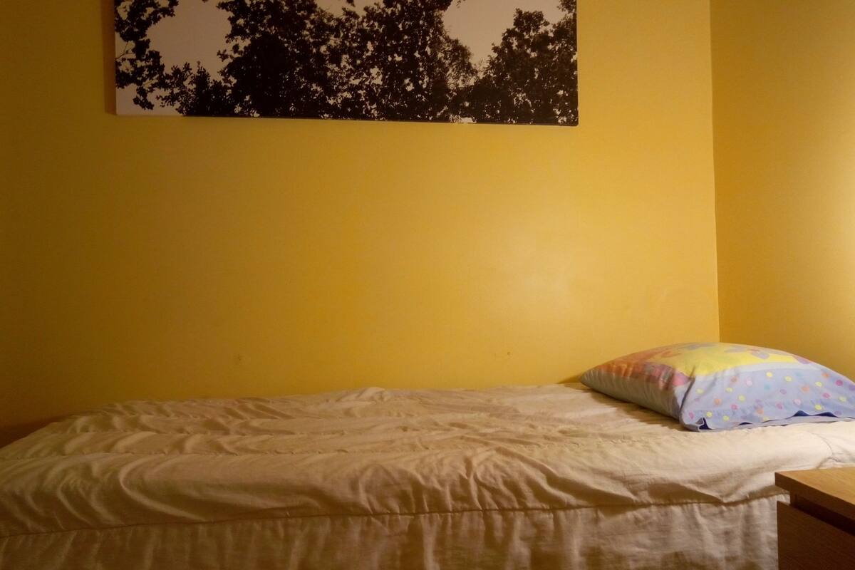 A bedroom with a bed, a bedside table, a lamp, and a wall-mounted picture.