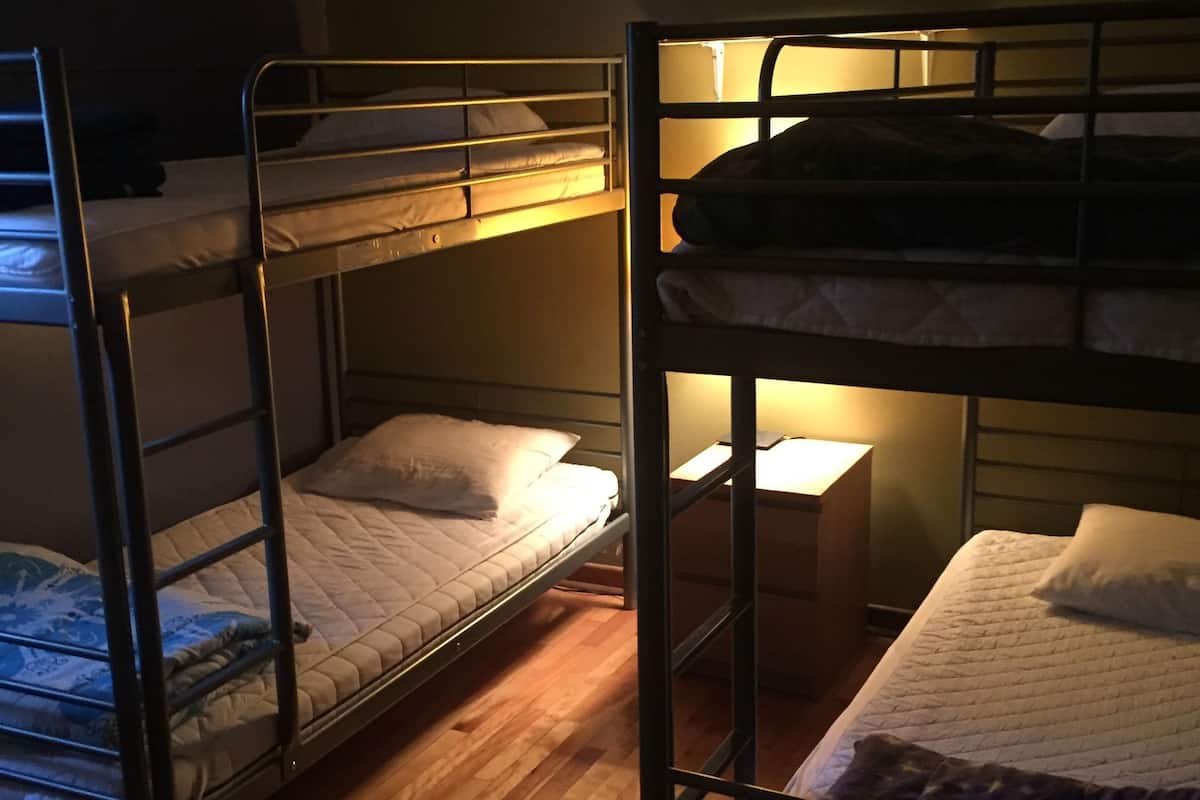 A dormitory room with bunk beds, a wooden floor, and a bedside table with a lamp.