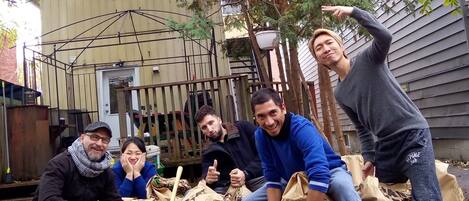 A group of people sitting on bags with text on them, in an outdoor setting with a house and a metal fence in the background.