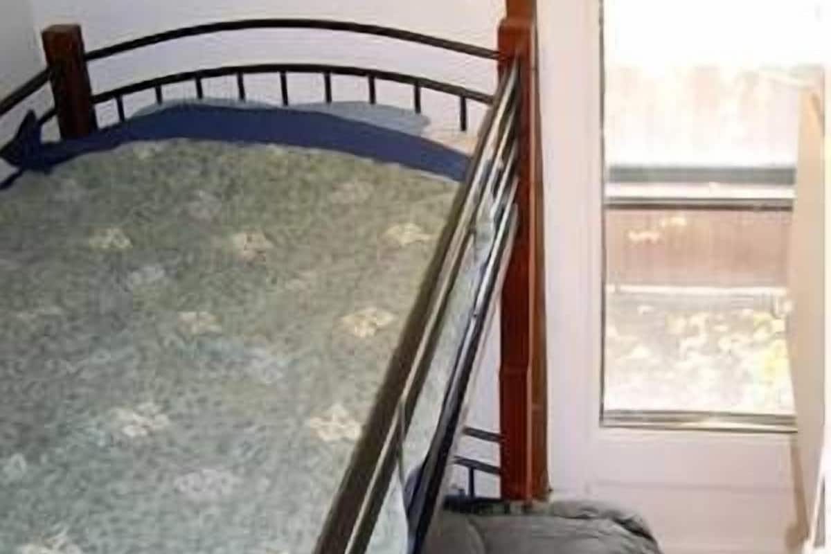 A bunk bed with a metal frame and a wooden headboard, a window with a view of the outside, and a door to the right.