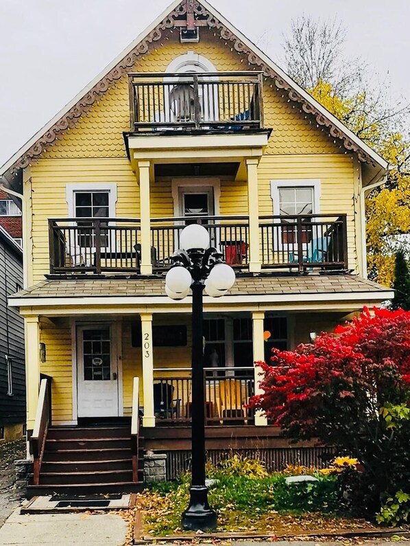A two-story yellow house with a balcony, a front door, and a street lamp.