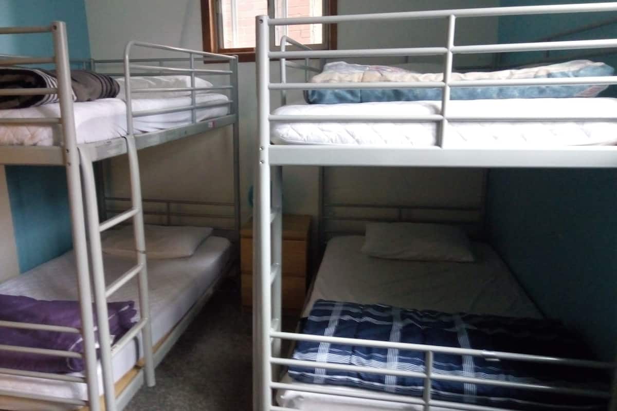 Two bunk beds with metal railings, a blue wall, and a window in the background.