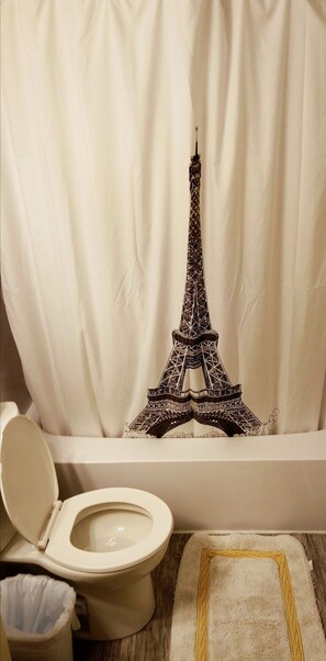 A bathroom with a toilet, a trash bin, and a shower curtain featuring a black and white Eiffel Tower design.