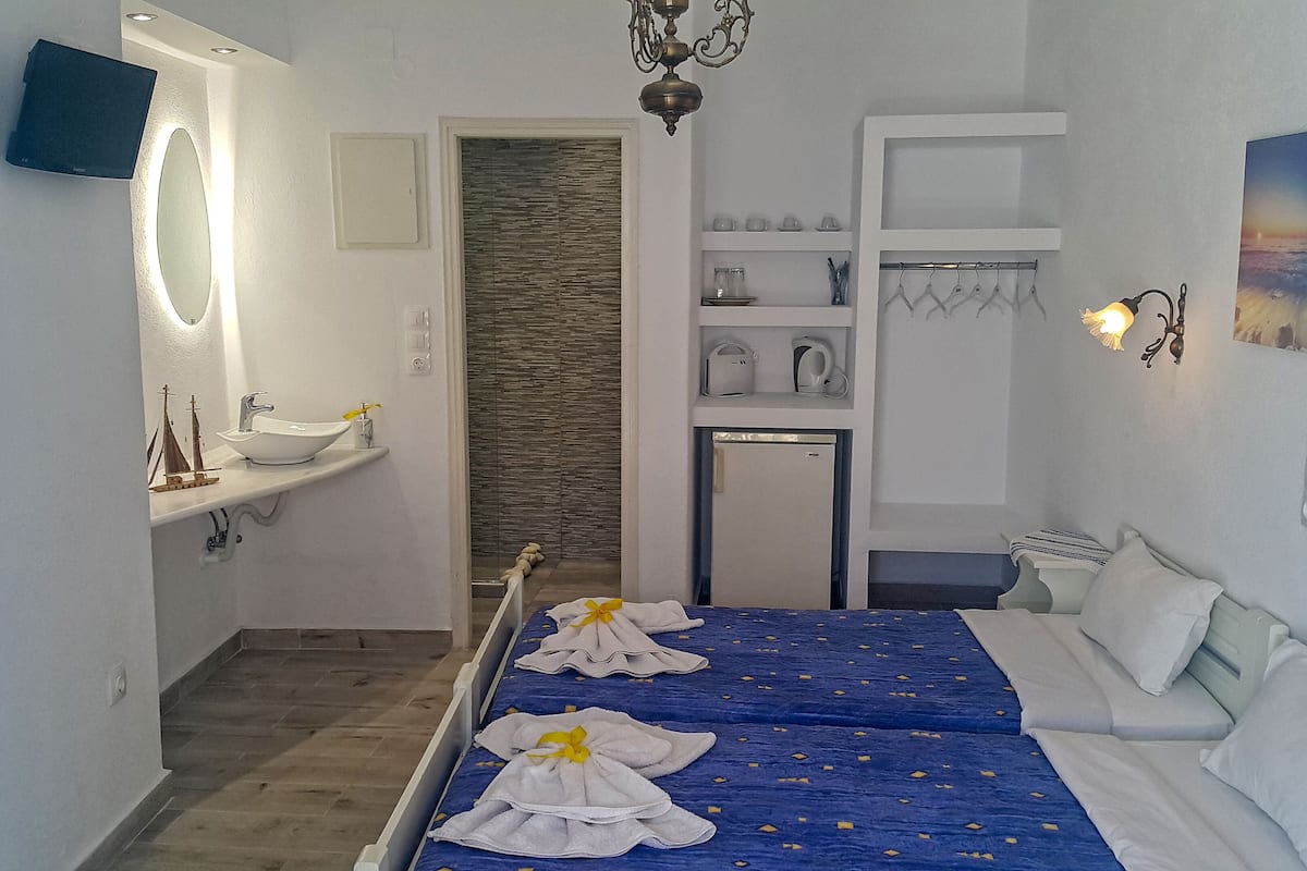 A hotel room with a bed, a bathroom with a sink and mirror, a small fridge, and a wall-mounted shelf with towels.
