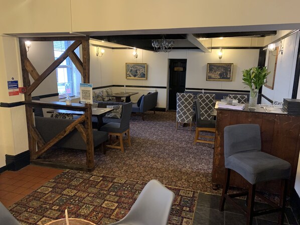 A restaurant with a rustic interior, featuring exposed wooden beams, patterned carpet, and a variety of seating options including booths and tables.