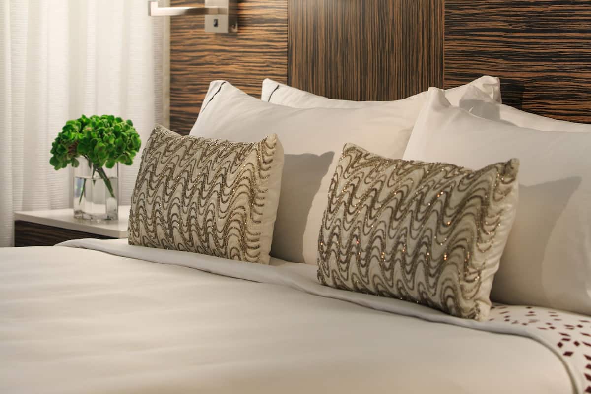 A hotel room with a neatly made bed, a wall-mounted lamp, and a large abstract painting above the bed.