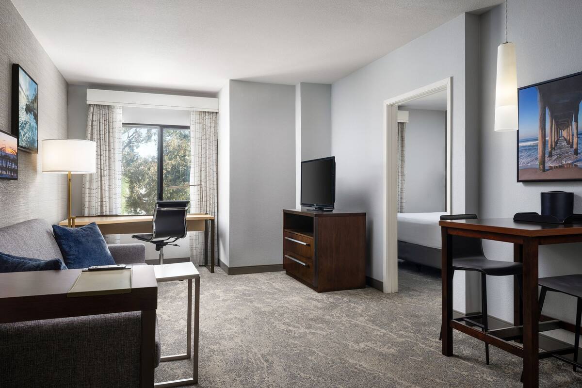 A hotel room with a sofa, a desk, a TV, and a dining area.