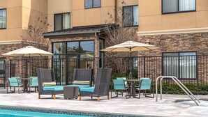 Un área junto a la piscina con sillones de descanso y sombrillas, un muro de piedra y un edificio con amplias ventanas.