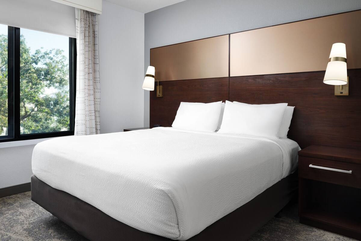 A neatly made bed with white linens, a wooden headboard, and two wall-mounted lamps.