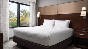 Una habitación de hotel con una cama grande, dos mesitas de noche y un ventanal con cortinas.