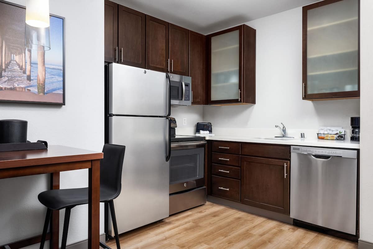 A modern kitchen with wooden cabinets, stainless steel appliances, a dishwasher, and a dining area with a table and chairs.