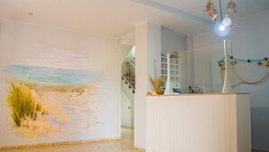 A reception area with a beach mural, a staircase, and a hanging light fixture. - Hostal Patio Andaluz (Punta Umbría)
