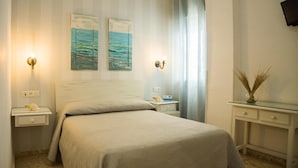A neatly arranged bedroom with a bed, bedside tables, a nightstand, and a small desk with a vase. - Hostal Patio Andaluz (Punta Umbría)