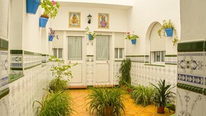 A corridor with tiled flooring, potted plants, and doors with windows. - Hostal Patio Andaluz (Punta Umbría)