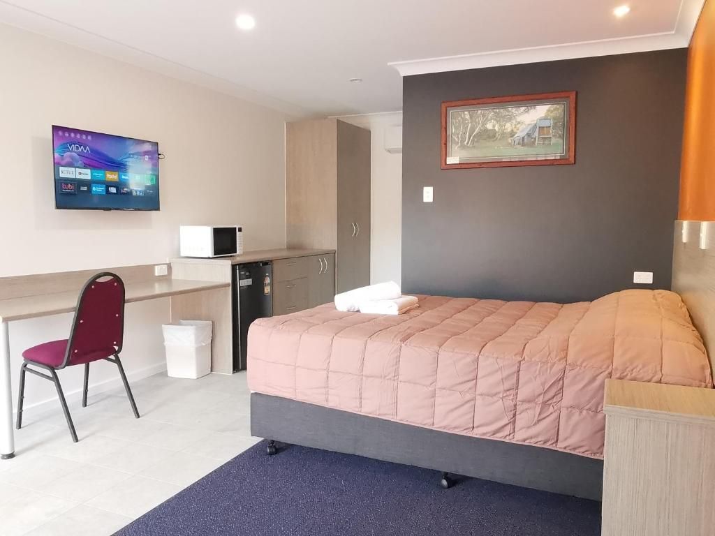 A hotel room with a bed, a desk, a chair, a TV, and a picture on the wall.