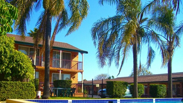 A hotel with a swimming pool, palm trees, and a two-story building with balconies. - Homestead Motel (Dubbo)