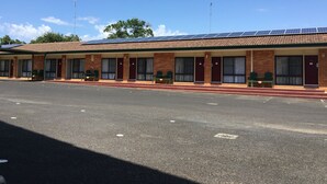 A motel with multiple rooms, each with a door and windows, and a covered parking area. - Homestead Motel (Dubbo)