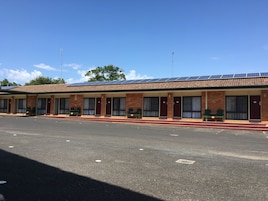 Un motel con varias habitaciones, cada una con puerta y ventanas, y un estacionamiento techado.
