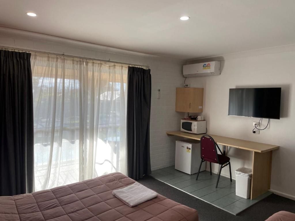A hotel room with a bed, a desk, a chair, a TV, an air conditioner, and a window with curtains.