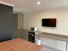 Habitación de hotel con cama, microondas, televisión, kitchenette pequeña y basurero.
