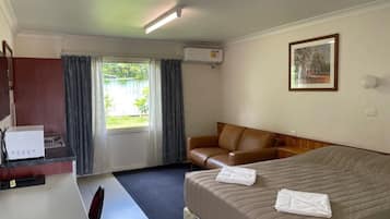 A hotel room with a bed, a desk, a chair, a sofa, and a window with curtains.