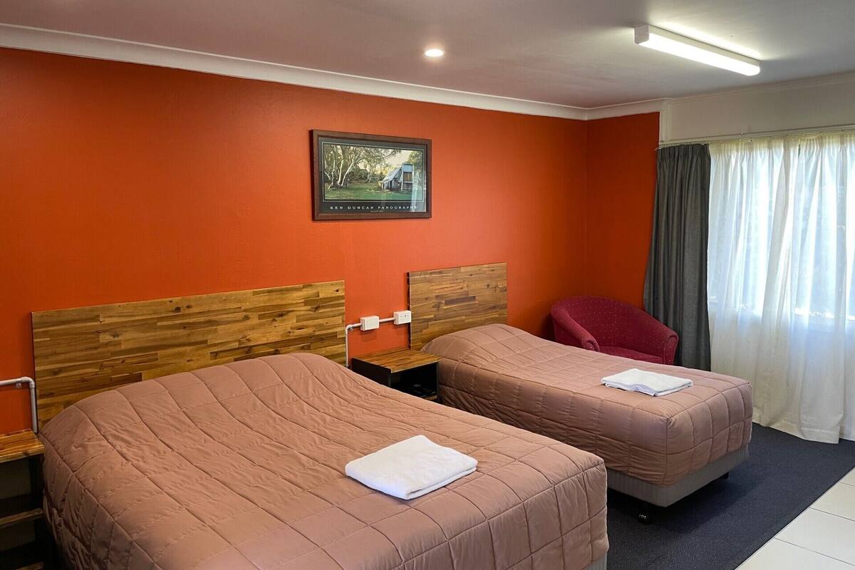 Quarto de hotel com duas camas, cabeceira de madeira, fotografia emoldurada na parede e janela com cortinas.