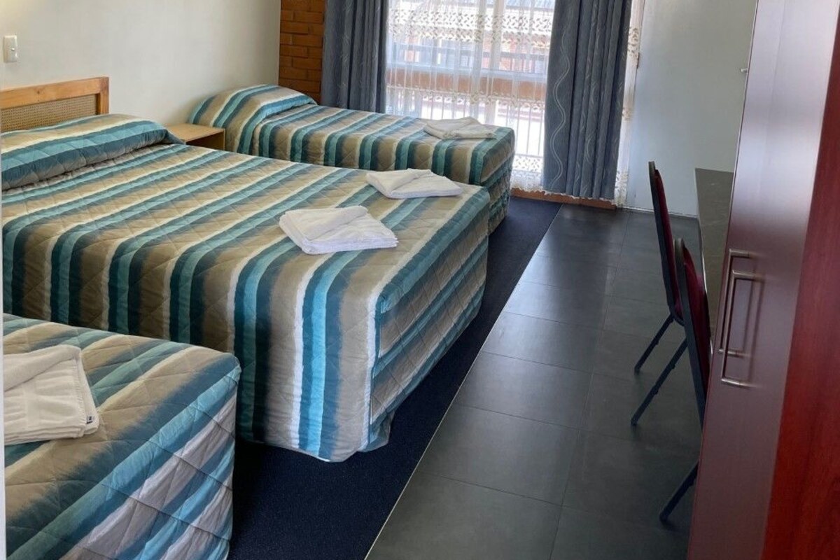 Une chambre d’hôtel avec deux lits, un mur décoratif en bois, une fenêtre avec des rideaux, une porte et une petite table.