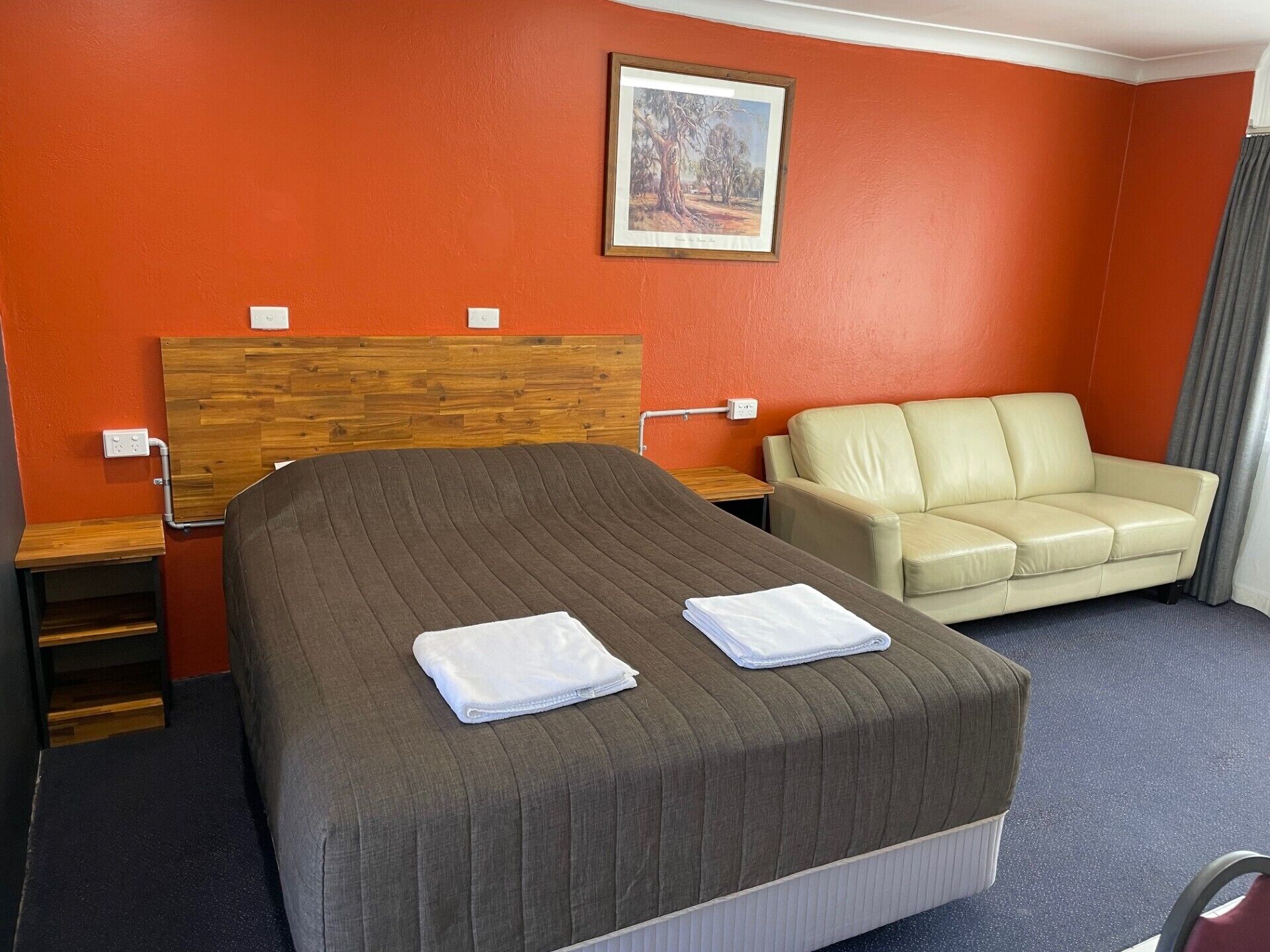 A hotel room with a bed, a sofa, a painting on the wall, and a window with curtains.