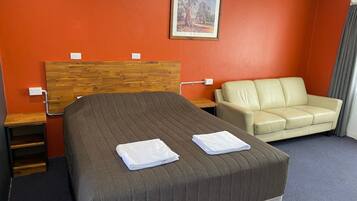 A hotel room with a bed, a sofa, a painting on the wall, and a window with curtains.