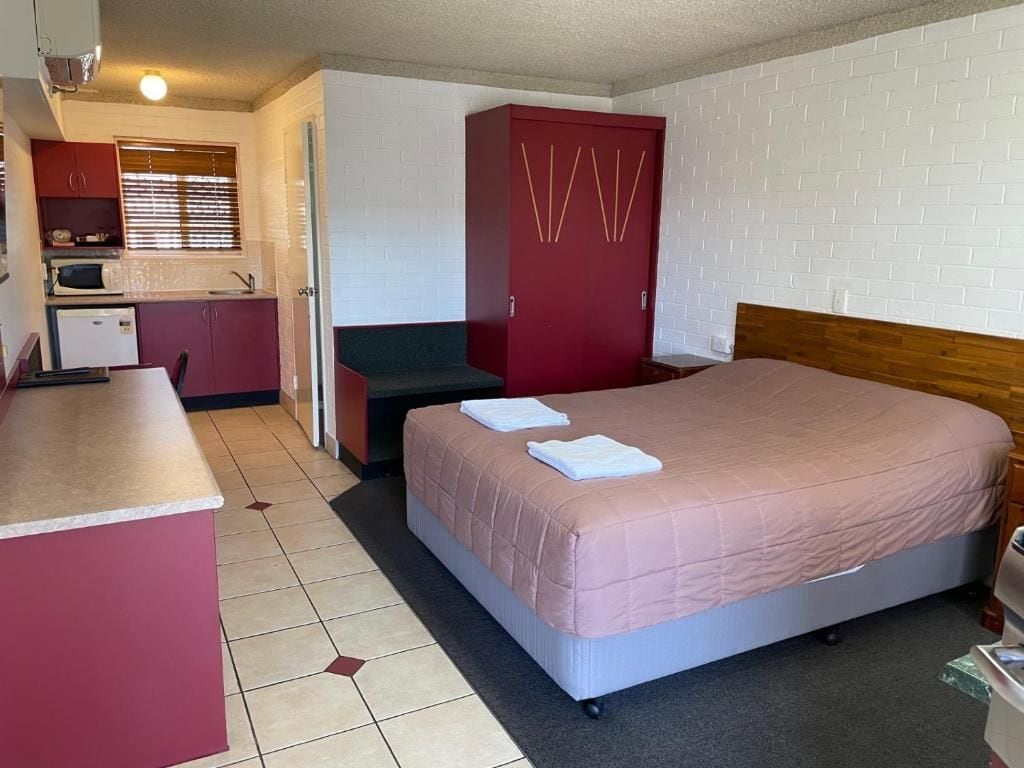 A compact room with a bed, a kitchenette, and a red wardrobe.