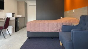 A compact hotel room with a bed, a desk, a chair, and a microwave. - Homestead Motel (Dubbo)