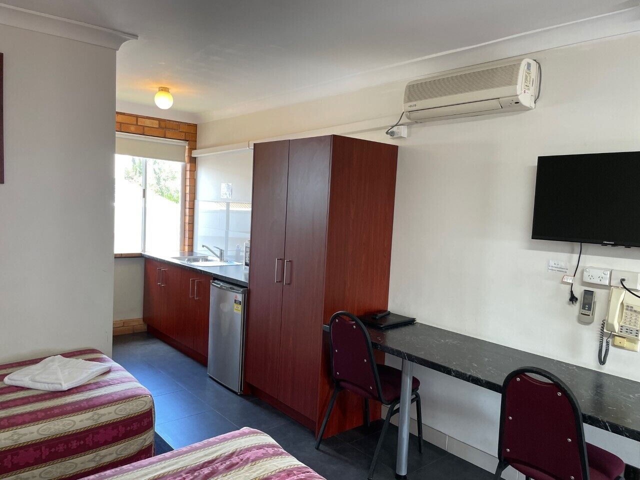 A compact kitchen with a refrigerator, wooden cabinets, and a dining area with two chairs.