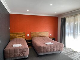 Una camera d'albergo con due letti singoli, una parete decorata in mattoni, una testata del letto in legno, una finestra con tende e un pavimento in moquette.