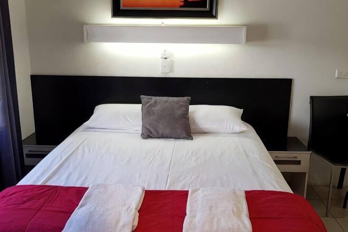Hotellihuone, jossa on sänky, yöpöytä, televisio ja seinään kiinnitetty valaisin.