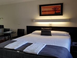 A hotel room with a bed, a desk, and a chair. There is a painting on the wall above the bed. - Motel Lodge (Allenstown)