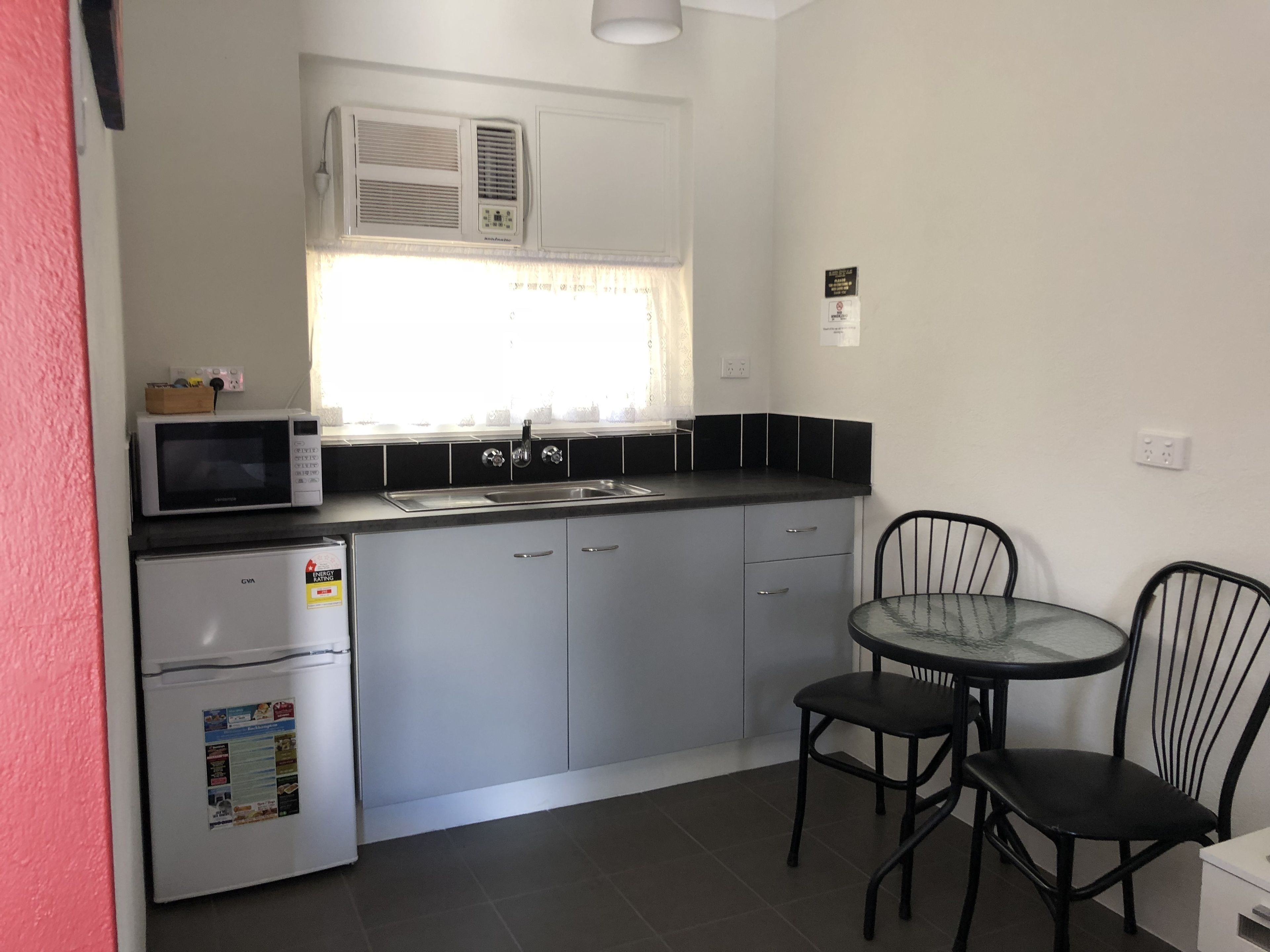 A compact kitchen with a microwave, refrigerator, sink, and a small dining area with two chairs and a table.