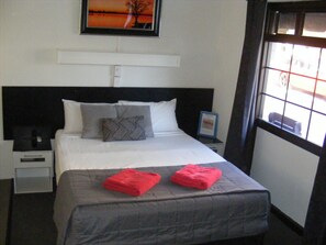 A neatly made bed with two red towels, a black and white patterned pillow, and a framed picture above it. - Motel Lodge (Allenstown)