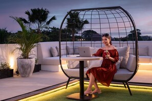 A woman in a red dress sitting on a white sofa with a laptop and a glass of red wine. - ABISHA Hotel Sanur (Denpasar)